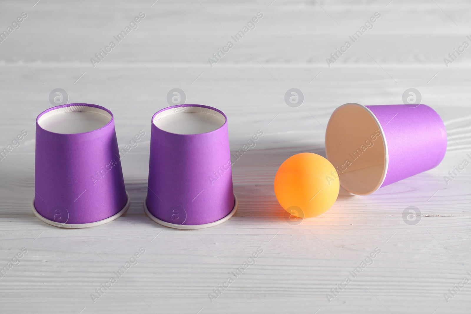 Photo of Shell game. Three purple cups and ball on white wooden table