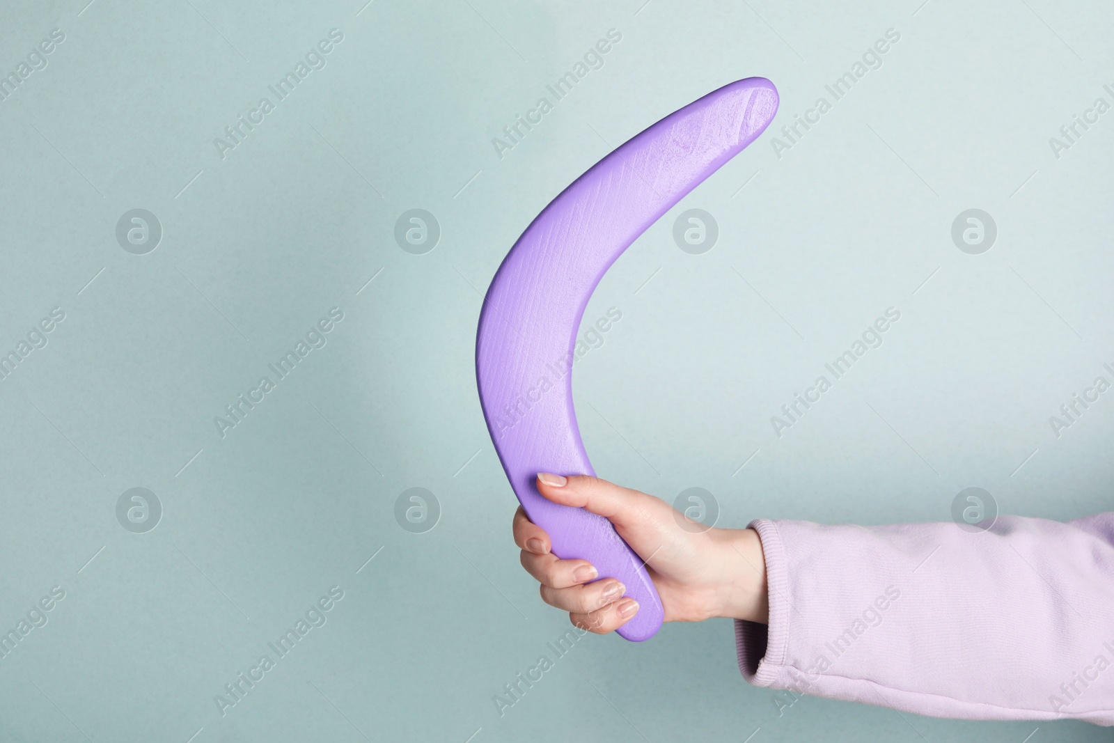 Photo of Woman holding boomerang on light grey background, closeup. Space for text