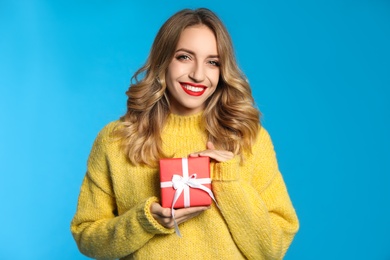 Happy young woman with Christmas gift on light blue background