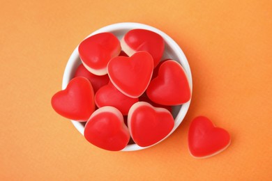 Photo of Bowl and delicious heart shaped jelly candies on orange background, flat lay
