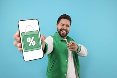 Image of Discount, offer, sale. Man pointing at mobile phone with illustration of bag and percent sign on screen, light blue background