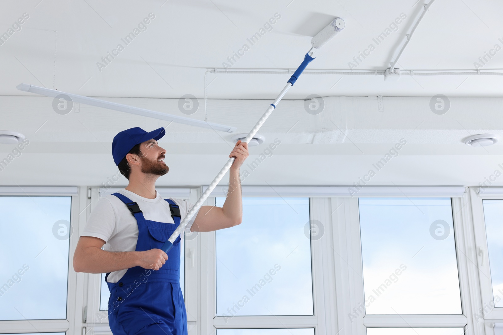 Photo of Handyman painting ceiling with roller in room