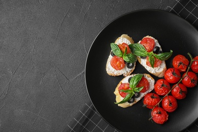 Photo of Plate of delicious tomato bruschettas on black background, top view. Space for text