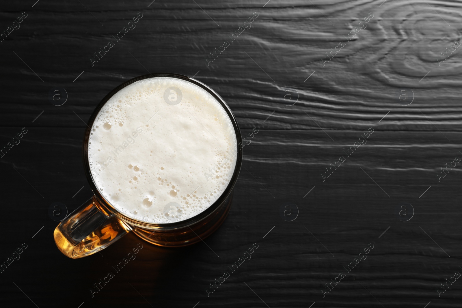 Photo of Glass mug with cold tasty beer on wooden background, view from above