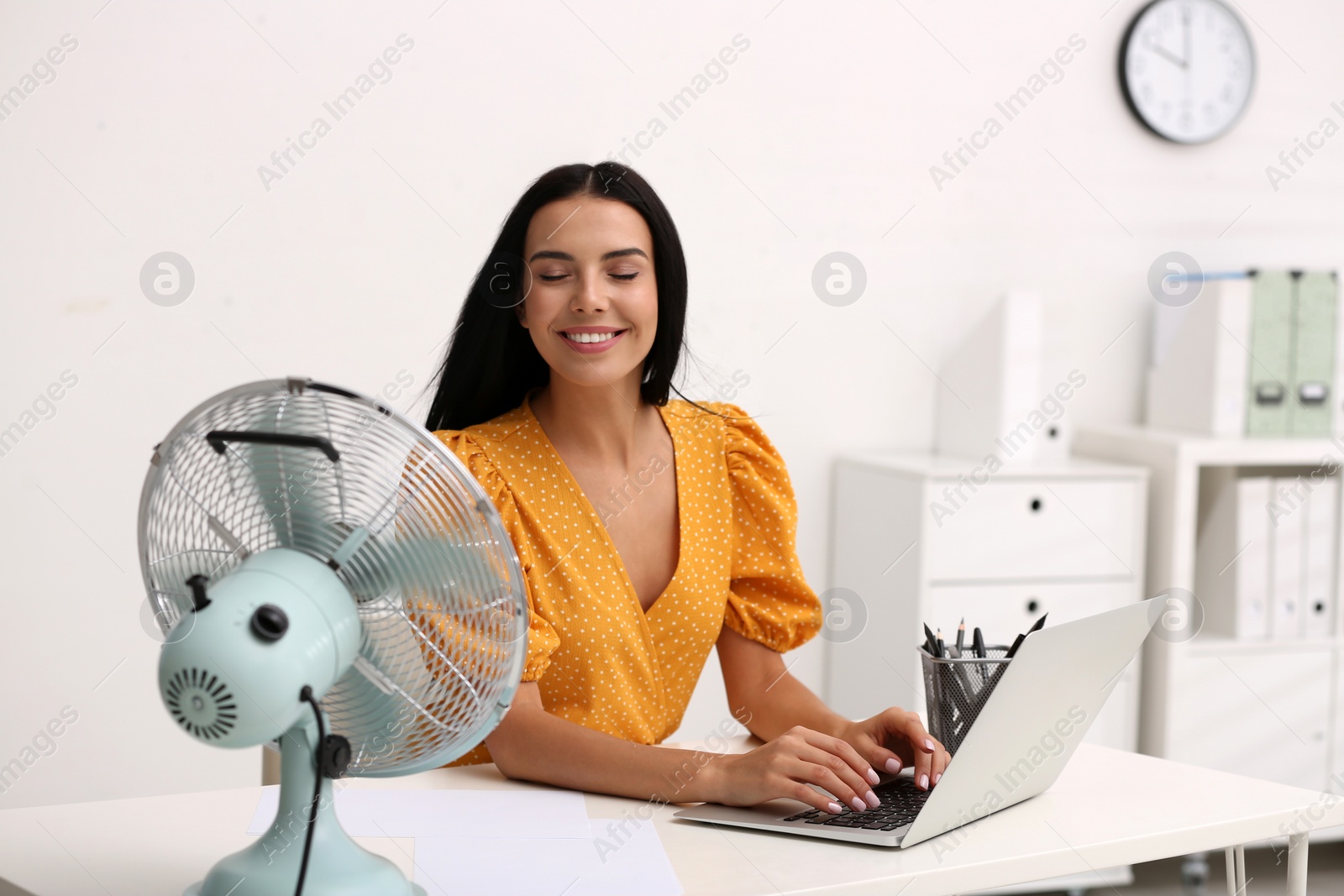 Photo of Young woman enjoying air flow from fan at workplace