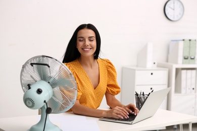 Young woman enjoying air flow from fan at workplace