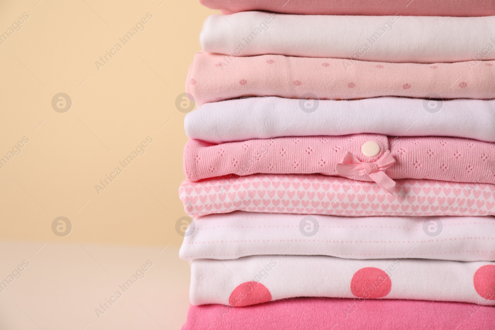 Photo of Stack of baby girl's clothes on yellow background, closeup. Space for text