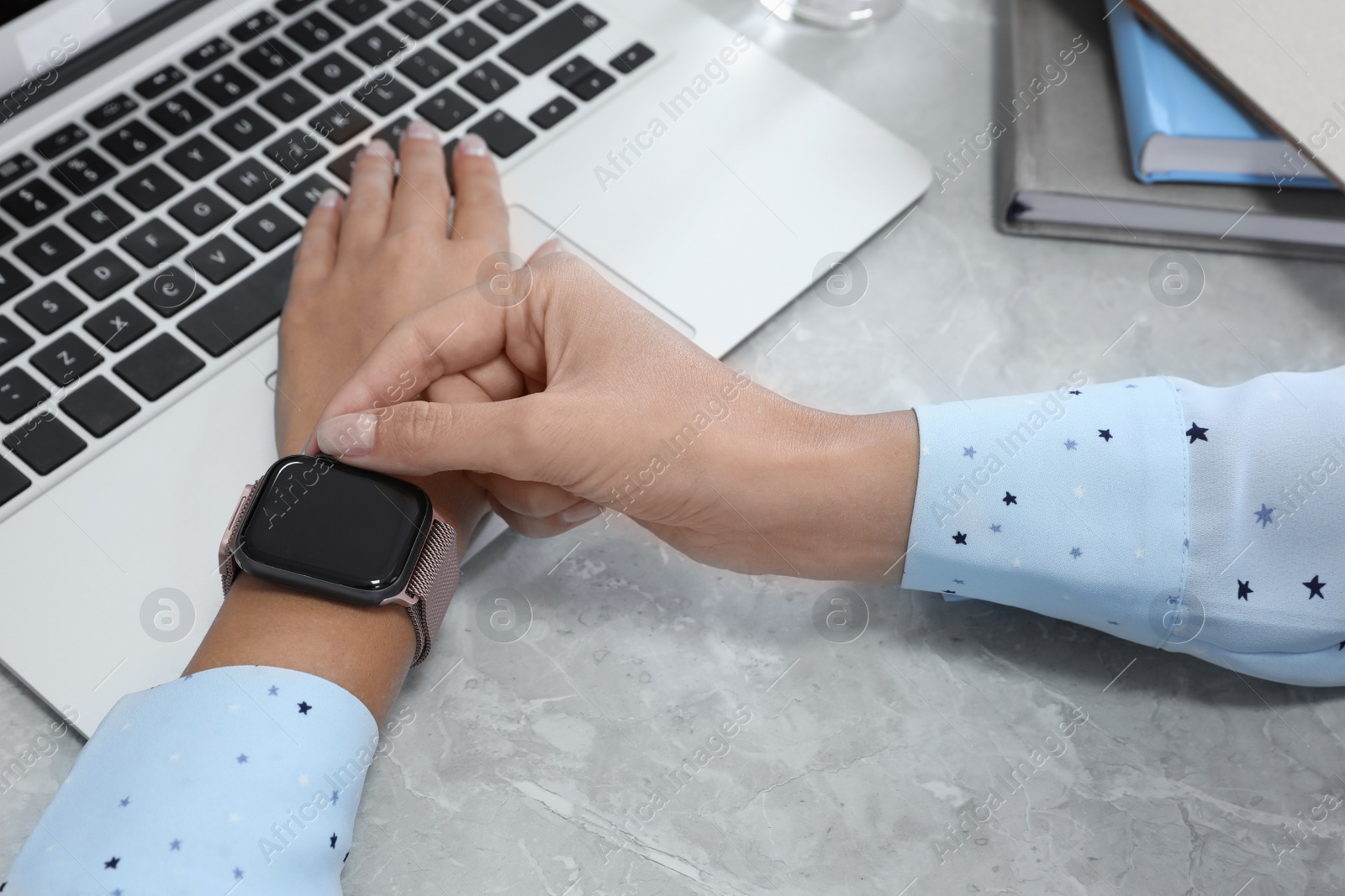 Image of Woman using stylish smart watch at grey marble table, closeup