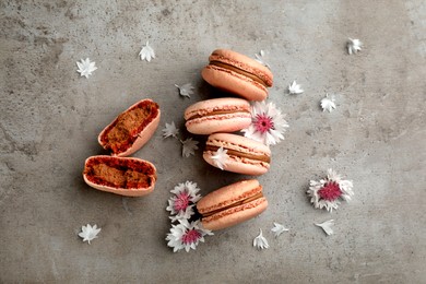 Delicious macarons and flowers on grey table, flat lay