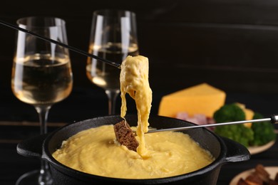 Photo of Dipping pieces of ham and bread into fondue pot with melted cheese on table, closeup