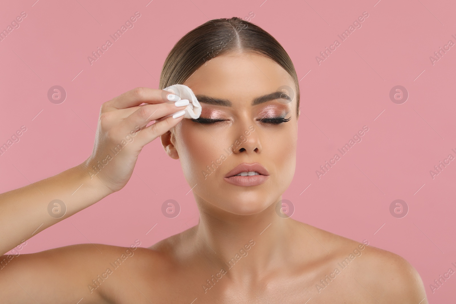 Photo of Beautiful woman removing makeup with cotton pad on pink background