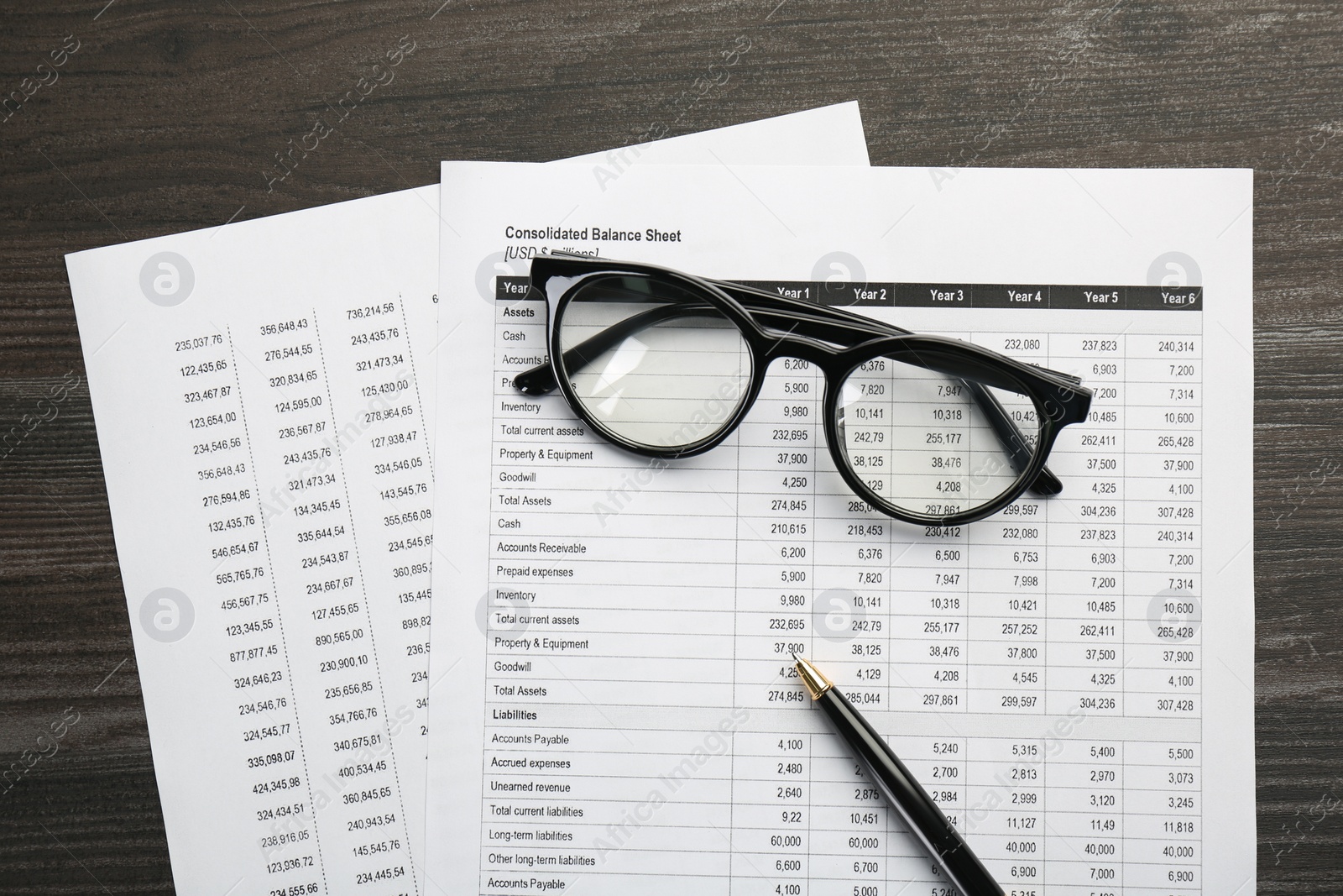 Photo of Accounting documents, glasses and pen on wooden table, top view