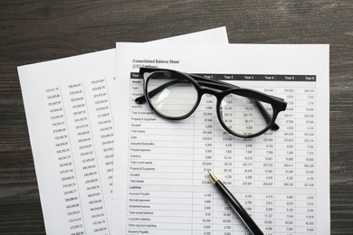 Accounting documents, glasses and pen on wooden table, top view