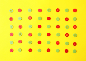 Photo of Many red and green sewing buttons on yellow background, flat lay