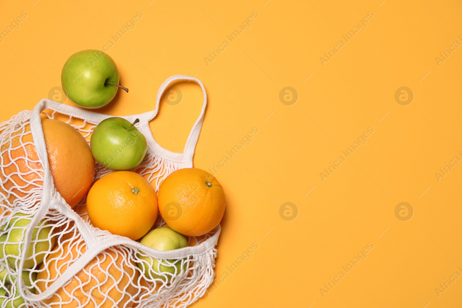 Photo of Fresh ripe fruits in net bag on orange background, flat lay. Space for text