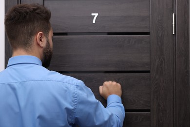 Collection agent knocking on wooden door, back view