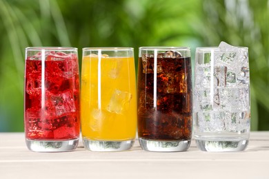 Photo of Glasses of different refreshing soda water with ice cubes on white wooden table outdoors