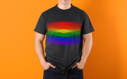 Young man wearing black t-shirt with image of LGBT pride flag on orange background