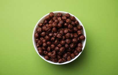 Photo of Chocolate cereal balls in bowl on green table, top view