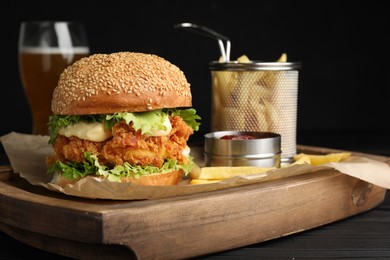 Photo of Delicious burger with crispy chicken patty, french fries and sauce on table