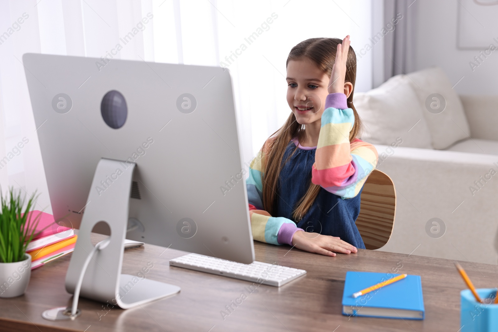 Photo of E-learning. Cute girl raising her hand to answer during online lesson at table indoors