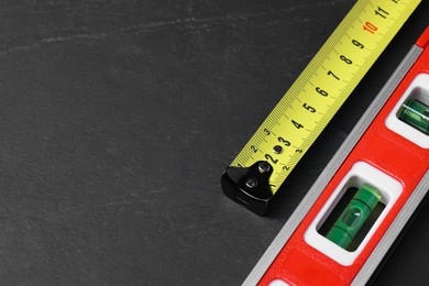 Building level and tape measure on black table. Space for text