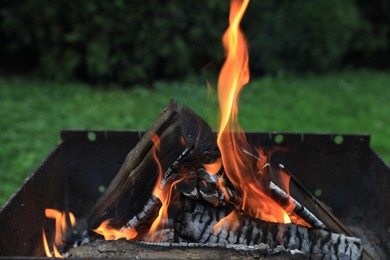 Metal brazier with burning firewood outdoors, closeup