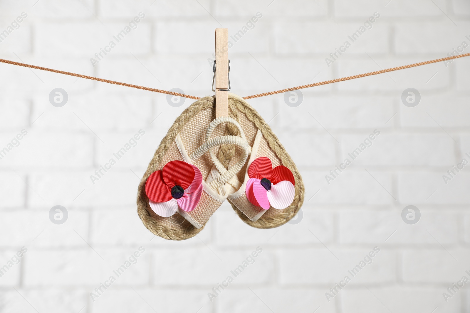 Photo of Cute baby shoes drying on washing line against white brick wall