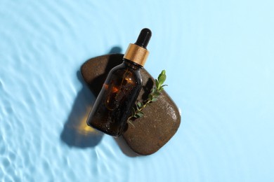 Photo of Bottle of cosmetic oil, leaves and stone in water on light blue background, top view