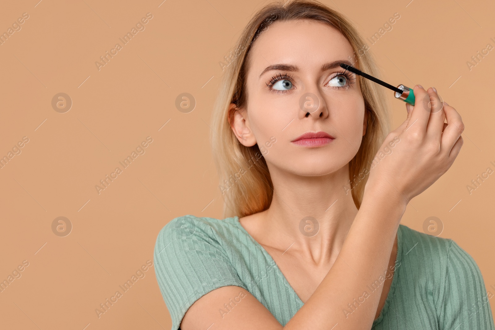 Photo of Beautiful woman applying mascara on beige background. Space for text