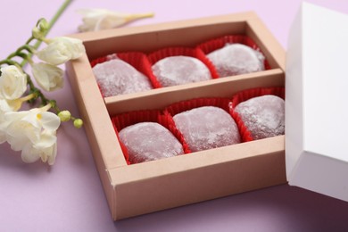 Box of delicious mochi and flowers on light background, closeup. Traditional Japanese dessert