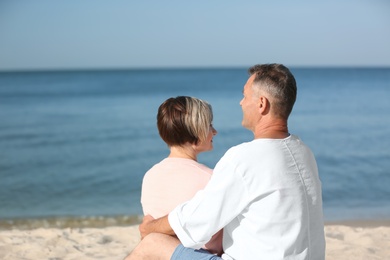 Happy mature couple sitting together at beach on sunny day