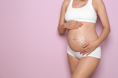 Sun painted with body cream on pregnant woman's belly against color background, closeup. Space for text