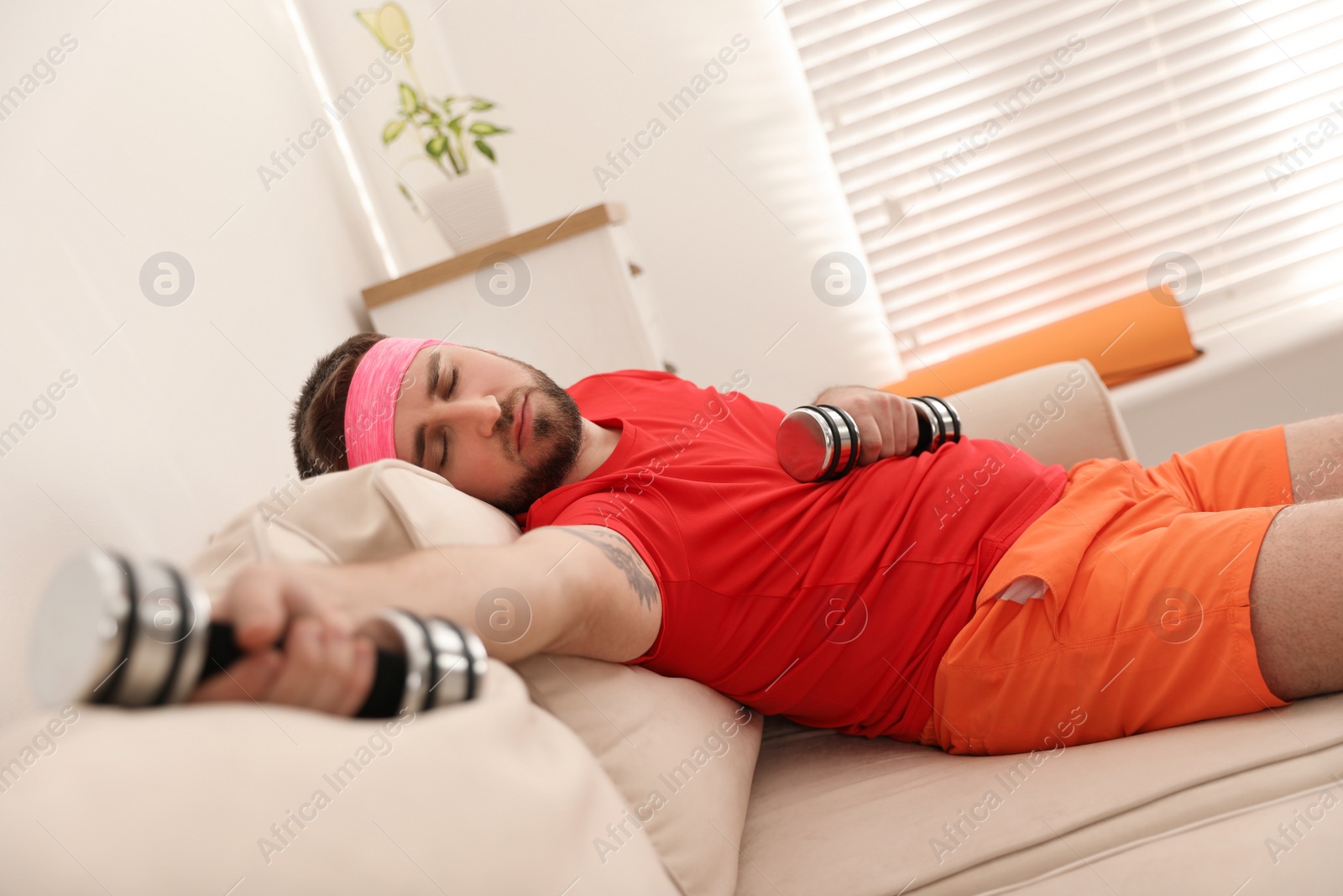 Photo of Lazy young man with sport equipment on sofa at home