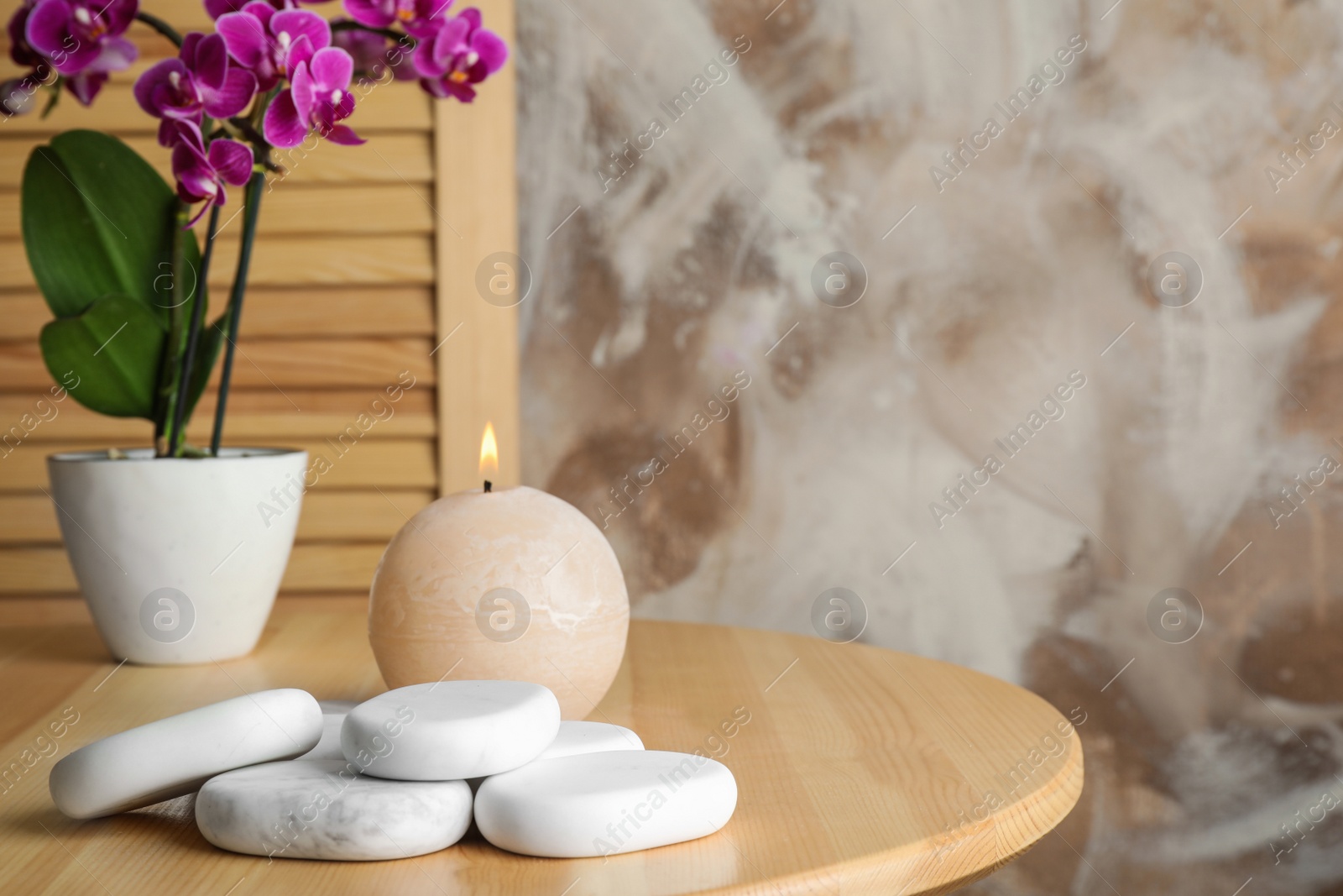 Photo of Spa stones, candle and blooming orchid indoors, space for text