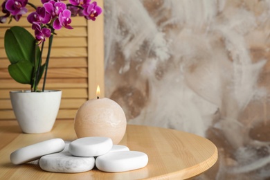 Photo of Spa stones, candle and blooming orchid indoors, space for text