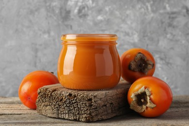 Photo of Delicious persimmon jam and fresh fruits on wooden table