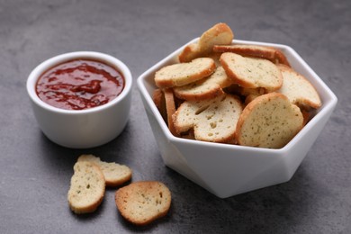 Photo of Crispy rusks and dip sauce on grey table, closeup