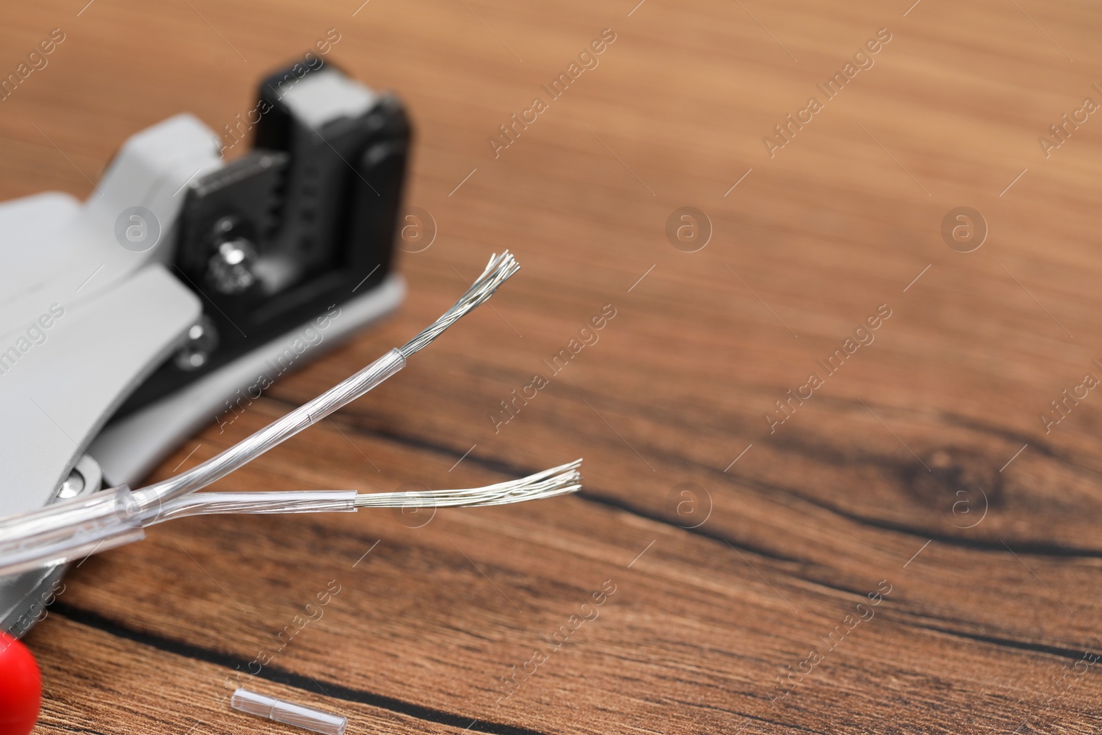 Photo of Cutters and stripped wire on wooden table, closeup. Space for text