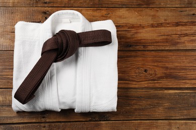 Photo of Brown karate belt and white kimono on wooden background, top view. Space for text