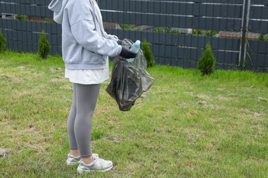 Woman with trash bag picking up plastic bottle outdoors, closeup. Recycling concept