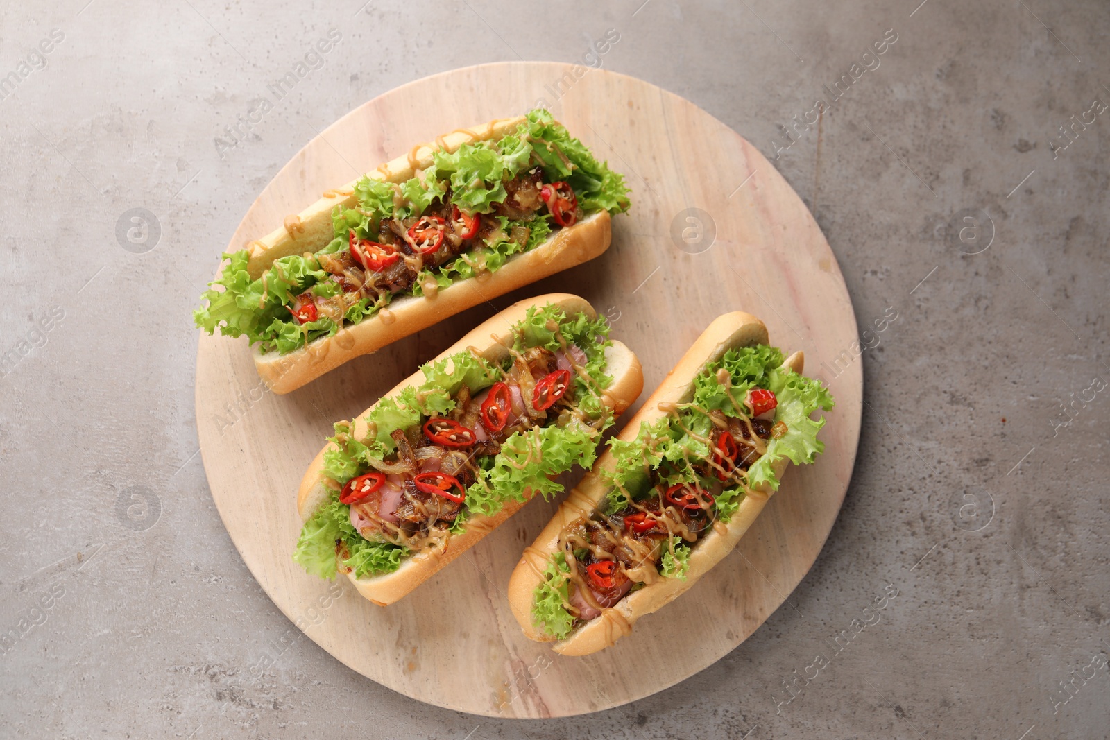 Photo of Tasty hot dogs with chili, lettuce and sauce on grey textured table, top view