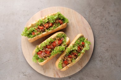 Tasty hot dogs with chili, lettuce and sauce on grey textured table, top view