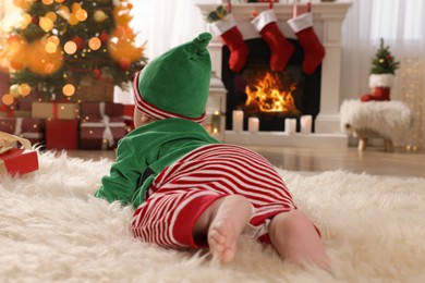 Photo of Baby wearing cute elf costume in room decorated for Christmas