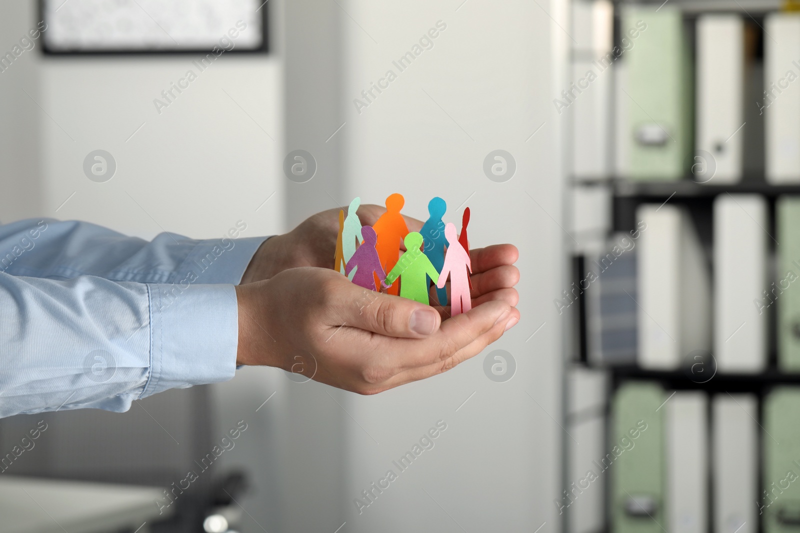 Photo of Man holding paper human figures in office, closeup. Diversity and Inclusion concept