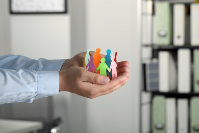 Man holding paper human figures in office, closeup. Diversity and Inclusion concept