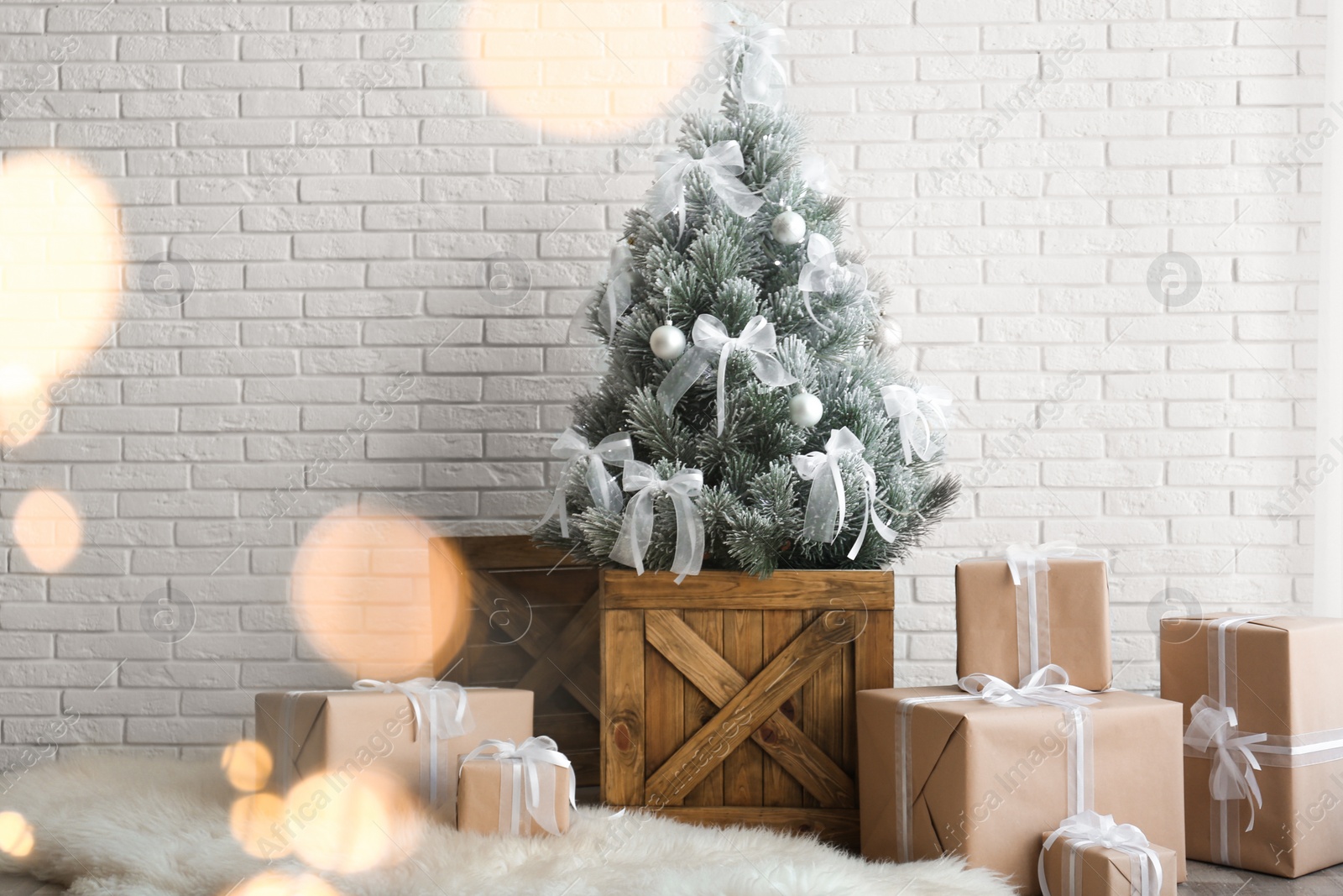 Photo of Stylish room interior with beautiful Christmas tree and gifts near white brick wall. Bokeh effect