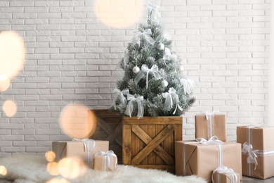 Stylish room interior with beautiful Christmas tree and gifts near white brick wall. Bokeh effect