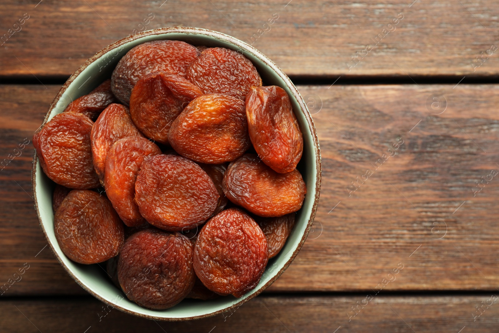 Photo of Bowl of tasty apricots on wooden table, top view and space for text. Dried fruits