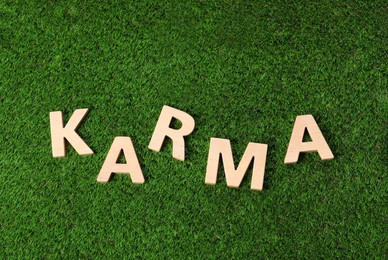 Photo of Word Karma made with wooden letters on green grass, top view